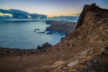 Fototapeta na wymiar Panoramic view from a steep cliff over the seascape and along the rugged foothills of Madeira coast at dawn. Ponta do Bode, Madeira Island, Portugal, Europe.