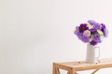 beautiful bouquet of asters in white jug on background white wall