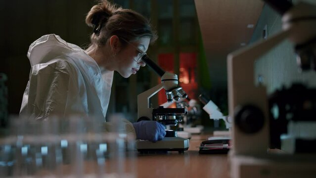 A young beautiful female scientist works with a professional microscope in the laboratory—medium shot.
