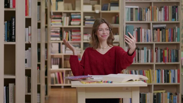 Studying female caucasian student in library takes video call on smartphone