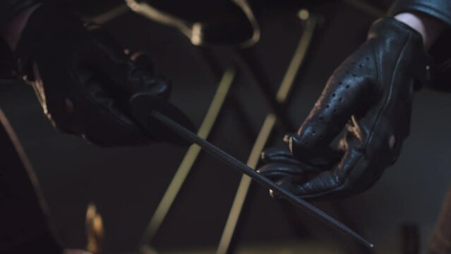 A person wearing black leather gloves holds a knife, tests its sharpness, and then places it in a holster.