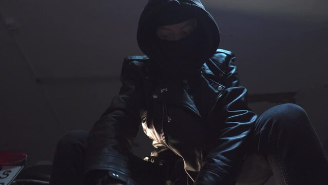 Criminal with bandit mask and black leather gloves inspects wrench, screw driver and duck tape.