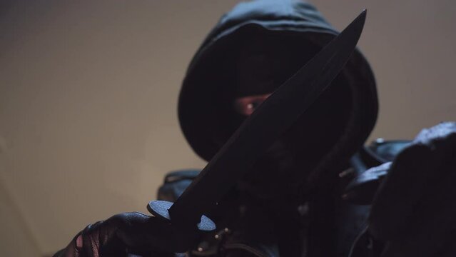 Robber with bandit mask and black leather gloves looking at knife and testing sharpness