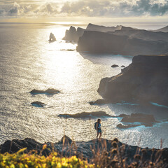 Backpacker woman enjoys hike at a steep cliff over the seascape and along the rugged foothills of...