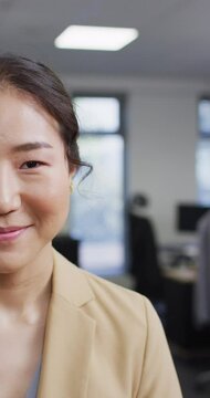 Vertical video of portrait of asian businesswoman looking at camera and smiling at office