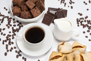 Delicious breakfast - aromatic coffee in a cup, milk jug, chocolate and cake cubes.