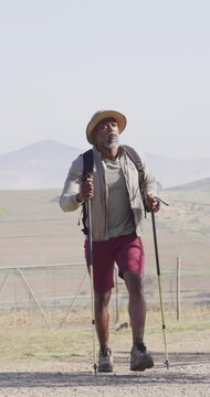 Vertical video of senior african american man hiking with trekking poles