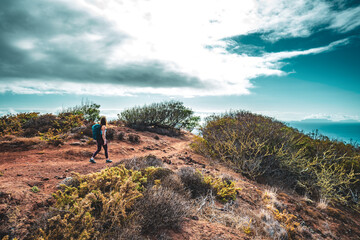 Backpacker woman enjoys hike along a steep cliff overlooking the sea and the rugged foothills of...