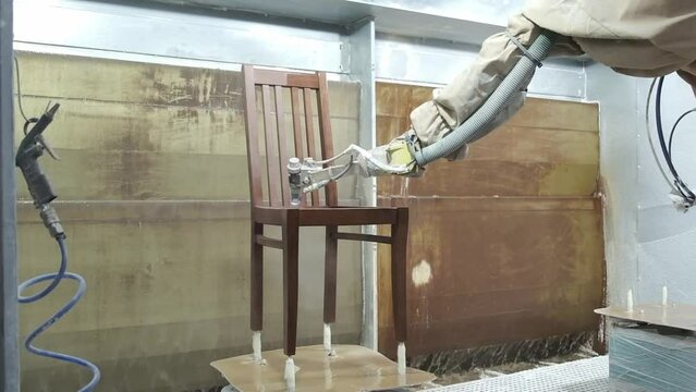 An automatic robotic arm paints a wooden chair