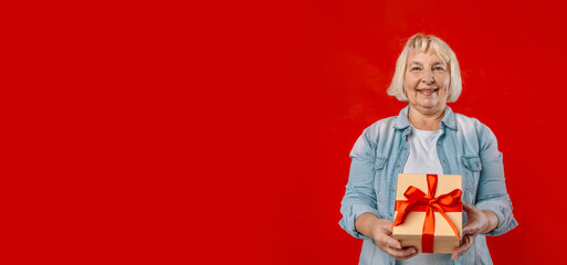 Happy 50s blonde woman hold shake red present box with gift ribbon bow isolated on plain red background studio portrait. 