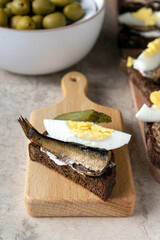 sandwich with sardine, egg, pickled cucumber on a wooden board, table setting