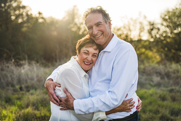 Senior couple hugging and smiling outside in backlight