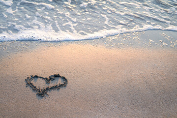 Heart drawn on the beach near foamy sea waves, empty space, copy space