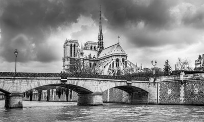 A black and white image of Notre Dame Cathedral in Paris France taken from the edge of the Seine River.