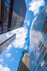 Looking up between the tall office buildings at the white clouds on a blue sky day in the financial district.