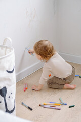One year child scribbling on white wall at home. Little kid drawing on walls by colored markers. Art therapy, normal development. 