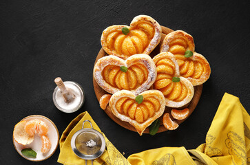 Puff pastry cake in the shape of a heart with tangerine slices on a wooden board on dark table with yellow napkin. top view, copy space