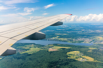 Fototapeta premium View of airplane wing, blue skies and green land during landing. Airplane window view.