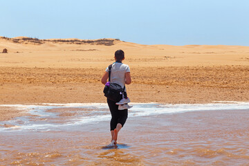 Unknown young woman crossing a shallow stream among african sandy landscape near Atlantic ocean...