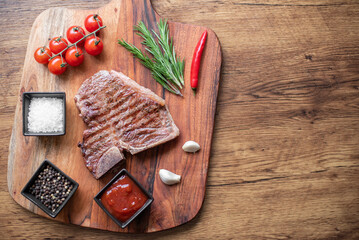 grilled T-bone steak on a cutting board with herbs on a wooden background with copy space for your text.