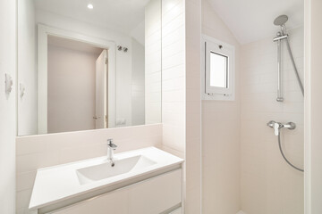 Petite but bright bathroom with shower, large mirror and sink, and a small window that gives some natural light. The clean white tiles and minimalistic design give the space a fresh and modern feel