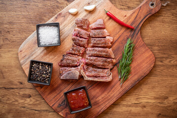 grilled T-bone steak on a cutting board with herbs on a wooden background