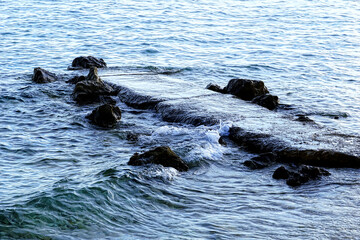 Natural stone pier splashing with sea waves on gloomy day
