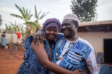 Two African people wearing traditional clothes hug each other during a celebration at the village.