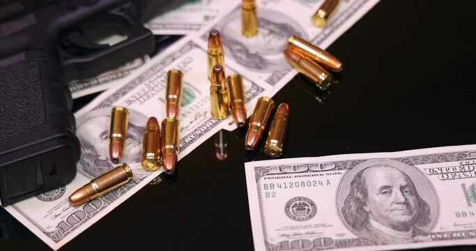Gun and bullets on dollar banknotes background, closeup shot. Criminal money. Black money and protection, mafia and corruption concept. Bills fall down - male hands count money or pay, slow motion