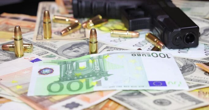 Gun and bullets on dollar and euro banknotes background, closeup shot. Criminal money. Black money and protection, mafia and corruption concept. Bills fall down slow motion