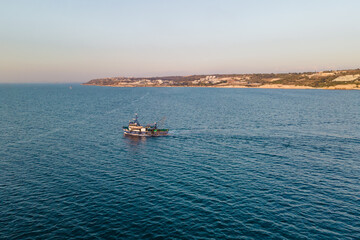 Fishing ship equipped with nets and a trawler sails through the azure water