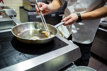 man chef cooking fried shrimp in frying pan on kitchen