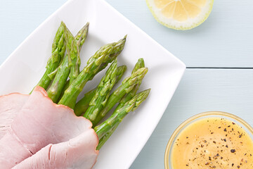 Fresh cooked green asparagus with ham slices, Hollandaise sauce on the side, photographed overhead...