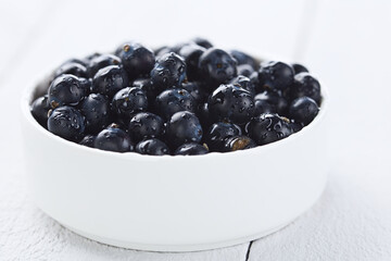 Fresh raw Patagonian Calafate berries (lat. Berberis heterophylla) in white bowl, photographed on white wood (Selective Focus, Focus one third into the berries)