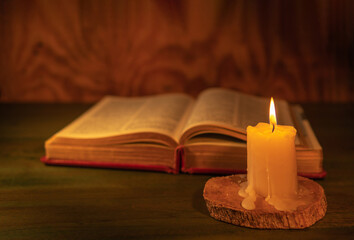 closeup of a lit candle with a bible on a wooden background