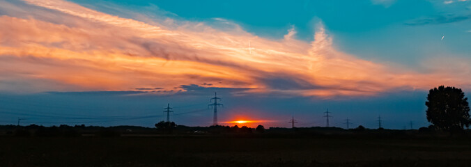 Beautiful sunset with a dramatic sky and overland high voltage lines near Tabertshausen, Bavaria, Germany