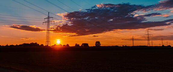 Beautiful sunset with a dramatic sky and overland high voltage lines near Tabertshausen, Bavaria, Germany