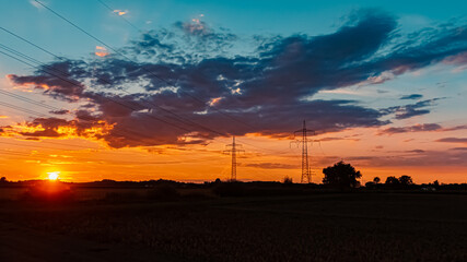 Beautiful sunset with a dramatic sky and overland high voltage lines near Tabertshausen, Bavaria, Germany