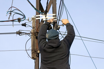 An electrician repairs power lines on a pole.