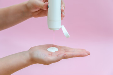 Woman's hand squeezing body lotion isolated on pink background. Beauty concept. Tube for cosmetic products