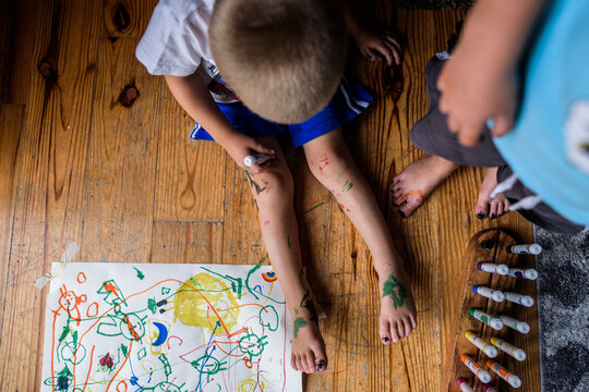 two children next to paper and markers with marker covering their legs