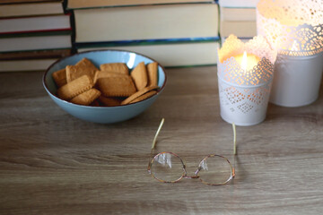 Glasses, bowl of biscuits, lit candles and books in the background. Selective focus.