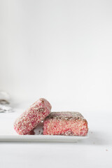 Pink lamingtons on a ceramic plate Australian raspberry lamingtons, small cakes covered in desiccated coconuts
