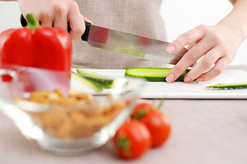 close-up beautiful female young hands cut cucumber with big knife on white porcelain board camera slowly floats shooting tomatoes peppers in glass dish beige background cooking delicious diet food