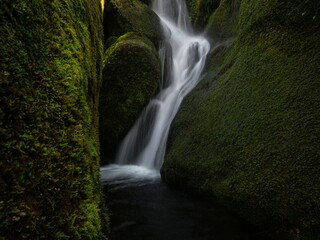 Long exposure of small freshwater river stream waterfall flowing through mossy rocks creek in Abel Tasman National Park