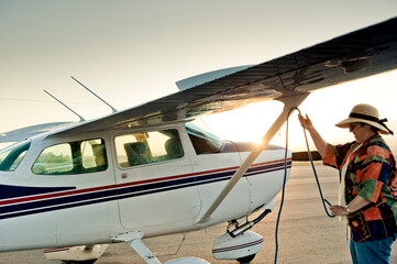 A woman ties down her small private plane as the sun sets.