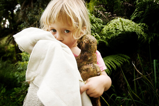 A young girl snuggles her blanket and stuffed dinosaur while hiking in the Waitomo Region of New Zealand.