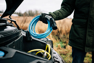 man putting an electric cable into the hood of an electric car