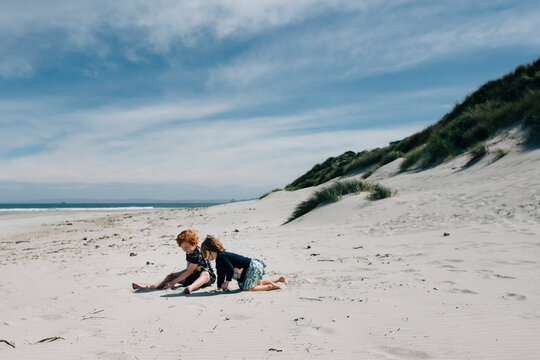 Full length of siblings playing with sand at beach against cloudy sky during sunny day