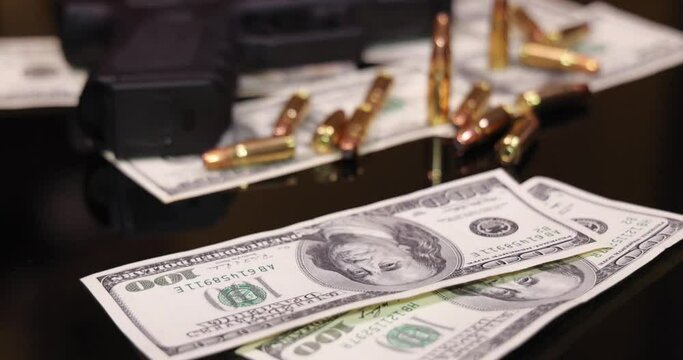 Gun and bullets on dollar banknotes background, closeup shot. Criminal money. Black money and protection, mafia and corruption concept. Bills fall down - count money or pay, slow motion